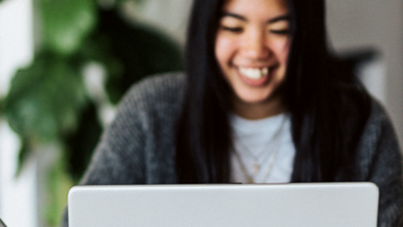 A woman smiles down at her laptop